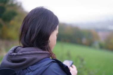 Bir kız akıllı telefonuna bakar, yumuşak, bulanık sonbahar manzarasına karşı durarak dijital hayat kavramını yakalar..