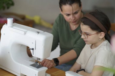 Bir anne kızına dikiş makinesinin ipliğini nasıl bağlayacağını ve dikiş dikeceğini gösterir. Eğitici ve yaratıcı çocuk konsepti.