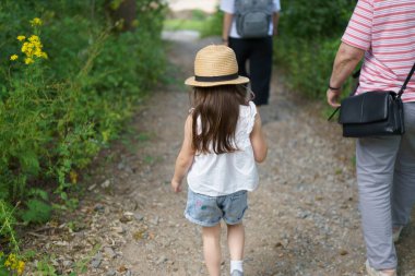 Bir yaz parkındaki patikada hasır şapkalı küçük bir kız. Çocukluk aktivitesi kavramı. Arkadan görüntüle.