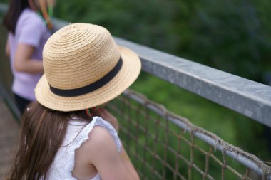 Küçük örgülü hasır şapkalı küçük bir kız bir yaz parkında yolda yürüyor. Çocukluk aktivitesi kavramı. Yan görünüm.