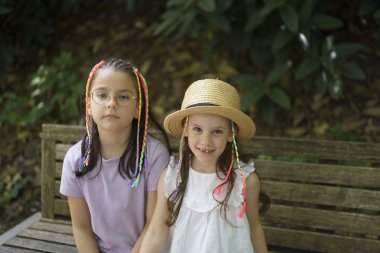 Hasır şapkalı küçük tatlı bir kız ve yaz yürüyüşü sırasında bankta oturan küçük renkli örgülü bir kız. Aktif bir çocukluk kavramı.