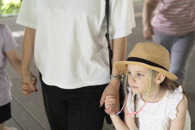 Beyaz gömlekli bir adamla el ele tutuşan bir kız, el ele tutuşan bir kadın ve çocuk. Hasır şapka takan bir çocuk ve bir kız. Şapka, saat, kulak ve bulanık bir gömlek. Siyah pantolonlu bir adam..