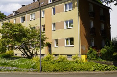 Sokak lambası olan bir bina, önünde bir ağaç. Çiçekli ya da çiçekli pencereler. Üzerinde logo olan sarı bir kutu. Pencerenin yakın çekimleri ve beyaz çerçeve.