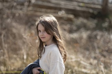 Gülümseyen kız elinde ceketle kameraya bakıyor. Çocukların boş zamanı ve duyguları kavramı.