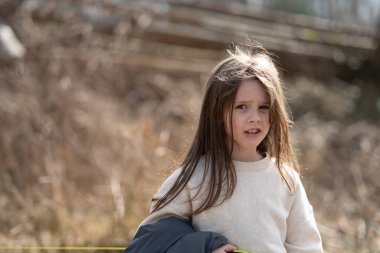 Gülümseyen kız elinde ceketle kameraya bakıyor. Çocukların boş zamanı ve duyguları kavramı.