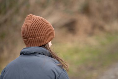 Kameraya arkası dönük, kahverengi şapkalı ve ceketli bir kız ormanda bir patikada. Çocukların yalnızlığı ve duyguları kavramı