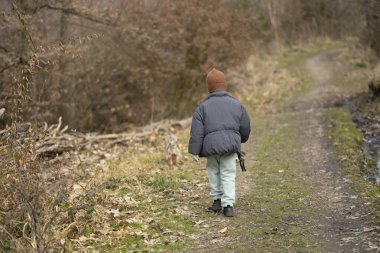 Kameraya arkası dönük, kahverengi şapkalı ve ceketli bir kız ormanda bir patikada. Çocukların yalnızlığı ve duyguları kavramı
