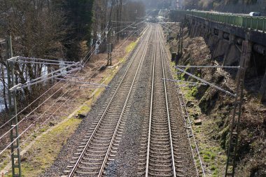 Taştan bir duvarın yanında elektrik hatları olan yakın plan bir tren yolu. Demiryolu taşımacılığı kavramı