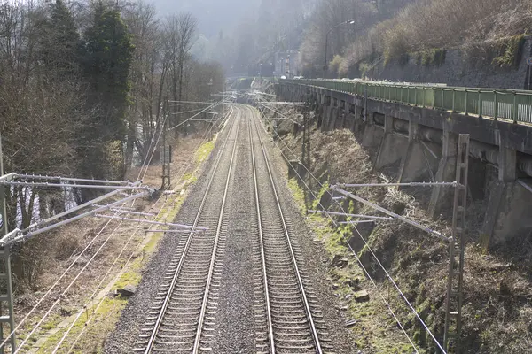 Taştan bir duvarın yanında elektrik hatları olan yakın plan bir tren yolu. Demiryolu taşımacılığı kavramı