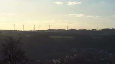 Tepedeki mavi gökyüzü arka planlı rüzgar türbini parkının 4k yatay videosu. Yenilenebilir enerji ve sürdürülebilir kalkınma kavramı