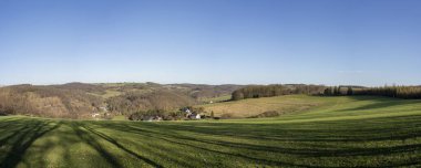 Baharda mavi gökyüzü ve ufukta bulutlar olan kırsal bölgelerin panoramik fotoğrafı. Alman manzara konsepti