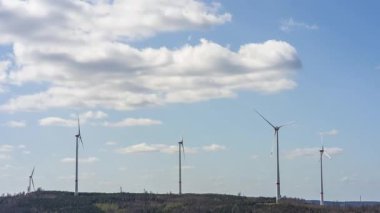 Tepedeki mavi gökyüzü arka planlı rüzgar türbini parkının 4k yatay zaman klibi. Yenilenebilir enerji ve sürdürülebilir kalkınma kavramı
