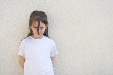 Duvarın yanında duran beyaz tişörtlü tatlı kız. akıllı çocuk kavramı çocuklar
