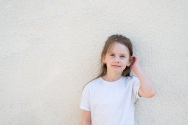 Duvarın yanında duran beyaz tişörtlü tatlı kız. akıllı çocuk kavramı çocuklar