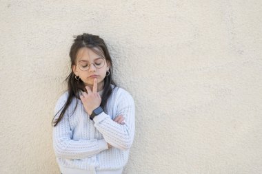 Kırmızı gözlüklü güzel kız kollarını kavuşturarak duvarın yanında duruyor. Eğitimsel çocukların akıllı çocuk kavramı