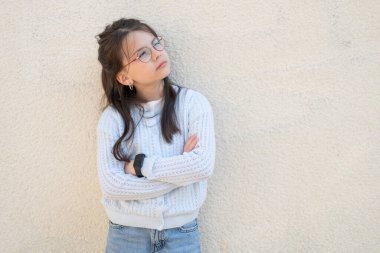Kırmızı gözlüklü güzel kız kollarını kavuşturarak duvarın yanında duruyor. Eğitimsel çocukların akıllı çocuk kavramı