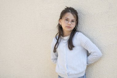 Kırmızı gözlüklü güzel kız kollarını kavuşturarak duvarın yanında duruyor. Eğitimsel çocukların akıllı çocuk kavramı