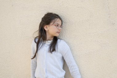 Duvarın yanında kameraya bakmayan gözlüklü tatlı kız. Eğitimsel çocuk konsepti