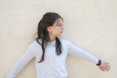 Gözlüklü, kolları açık, duvarın yanında duran tatlı bir kız. Eğitimsel çocuk konsepti