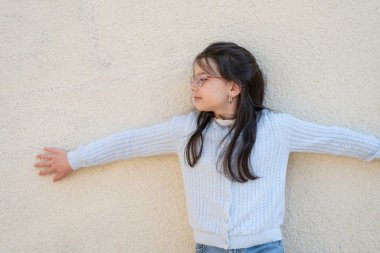 Gözlüklü, kolları açık, duvarın yanında duran tatlı bir kız. Eğitimsel çocuk konsepti