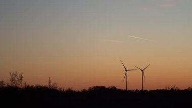 Gün batımında iki rüzgar türbini siluetinin 4K gerçek zamanlı videosu. Yeşil enerji ve ekoloji kavramı