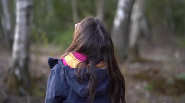 Ormanda duran gözlüklü ve ceketli genç bir kızın 4K gerçek zamanlı videosu. Mutlu çocuk konsepti
