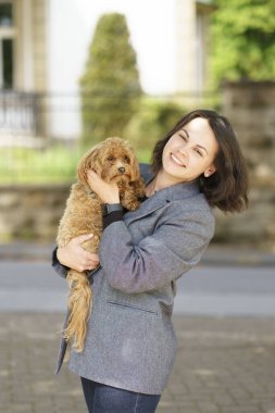 Gri ceketli ve kot pantolonlu güzel bir kadın elinde sevimli bir köpek yavrusu tutuyor. Köpek ve insan ilişkileri kavramı