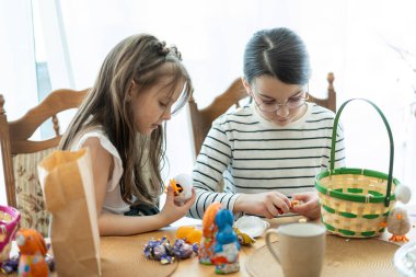 Tahta bir masada oturan iki kız sepetten toplanan Paskalya şekerlerini düzenliyor. Çocukların dini bayram kavramı