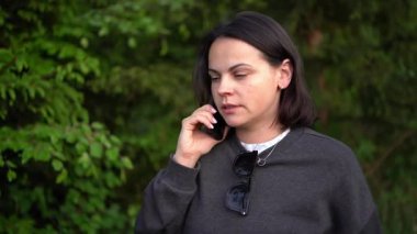Eşofmanlı ve kot pantolonlu bir kız ormanda cep telefonuyla konuşuyor. 4k gerçek zamanlı video