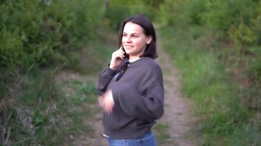 Eşofmanlı ve kot pantolonlu bir kız ormanda cep telefonuyla konuşuyor. 4k gerçek zamanlı video