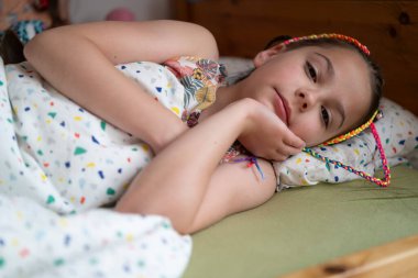 Renkli rastalı küçük kız battaniyenin altında yatakta yatıyor. Çocuk sabahı ve rutini kavramı