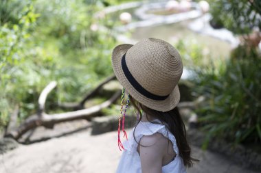 Çok renkli rastalı ve hasır şapkalı yalnız kız yazın parkta duran mesafeye bakıyor. Yüzü olmayan fotoğraf. Çocukların duyguları ve boş vakitleri kavramı