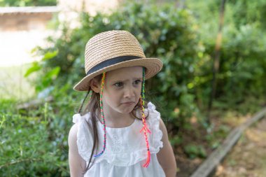 Hasır şapkalı ve çok renkli rastalı küçük kız ne yazık ki bir yaz parkında duruyor. Çocukluk yalnızlığı ve üzüntü kavramı