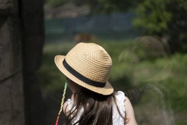 Hasır şapkalı kız, şeffaf bir bardağa yaslanmış, mesafeye bakıyor. Arkadan bak. Çocukluk merakı kavramı