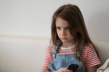 Uzaktan kumandayla kanepede yatan kot pantolonlu tatlı üzgün kız. Çocukların duyguları ve boş vakitleri kavramı