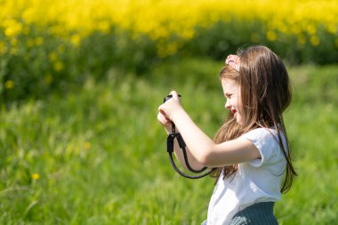 Elinde kamera olan küçük bir kız yaz tarlasında fotoğraf çekiyor. Çocukların yaratıcılığı ve rahatlığı kavramı
