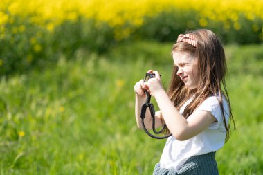 Elinde kamera olan küçük bir kız yaz tarlasında fotoğraf çekiyor. Çocukların yaratıcılığı ve rahatlığı kavramı