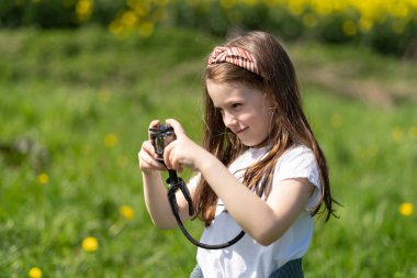 Elinde kamera olan küçük bir kız yaz tarlasında fotoğraf çekiyor. Çocukların yaratıcılığı ve rahatlığı kavramı