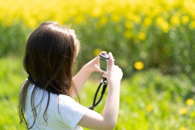 Elinde kamera olan küçük bir kız yaz tarlasında fotoğraf çekiyor. Çocukların yaratıcılığı ve rahatlığı kavramı