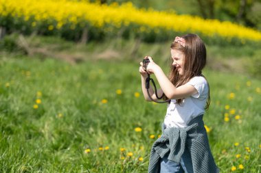 Elinde kamera olan küçük bir kız yaz tarlasında fotoğraf çekiyor. Çocukların yaratıcılığı ve rahatlığı kavramı