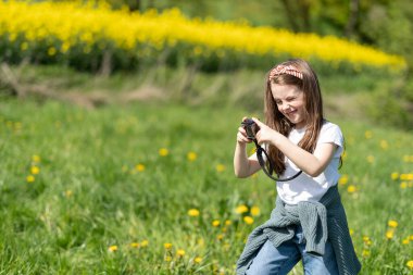 Elinde kamera olan küçük bir kız yaz tarlasında fotoğraf çekiyor. Çocukların yaratıcılığı ve rahatlığı kavramı