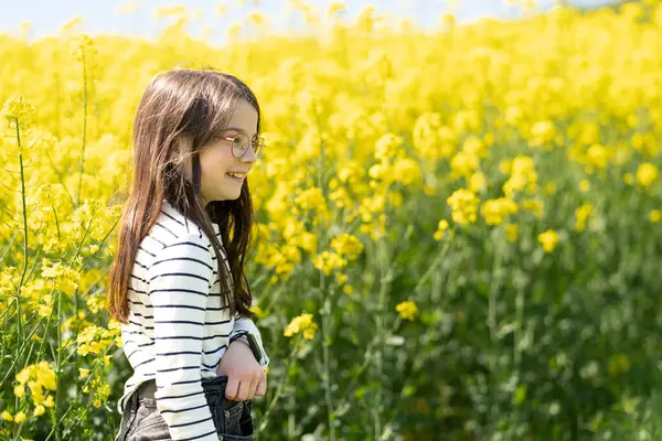 Gözlüklü ve çizgili tişörtlü şirin kız sarı kolza tohumu tarlasının önünde gülümsüyor. Çocukların duyguları ve boş vakitleri kavramı