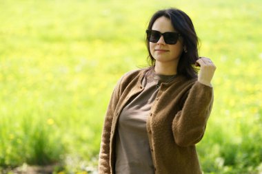 Güneş gözlüklü ve kahverengi kazaklı tatlı bir kız yazın tarlanın ortasında poz veriyor. Boş zaman ve aktivite konsepti