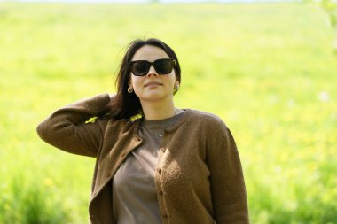 Güneş gözlüklü ve kahverengi kazaklı tatlı bir kız yazın tarlanın ortasında poz veriyor. Boş zaman ve aktivite konsepti