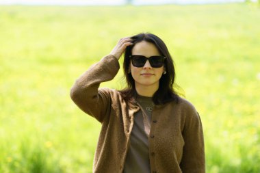 Güneş gözlüklü ve kahverengi kazaklı tatlı bir kız yazın tarlanın ortasında poz veriyor. Boş zaman ve aktivite konsepti