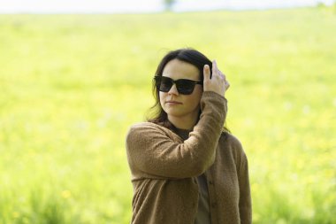 Güneş gözlüklü ve kahverengi kazaklı tatlı bir kız yazın tarlanın ortasında poz veriyor. Boş zaman ve aktivite konsepti