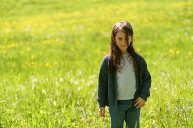 Kazaklı, kot pantolonlu, gücenmiş küçük bir kız bir tarlanın ortasında duruyor. Çocukluğun zorlukları kavramı.
