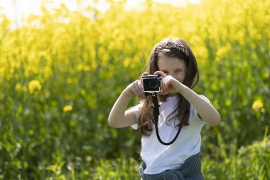 Elinde kamera olan küçük bir kız yaz tarlasında fotoğraf çekiyor. Çocukların yaratıcılığı ve rahatlığı kavramı