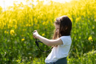 Elinde kamera olan küçük bir kız yaz tarlasında fotoğraf çekiyor. Çocukların yaratıcılığı ve rahatlığı kavramı