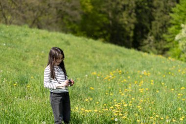 Uzun saçlı, gözlüklü ve çizgili tişörtlü güzel bir kız baharda sarı kolza tohumu tarlasının önünde fotoğraf çekiyor. Çocukların yaratıcılığı ve rahatlığı kavramı